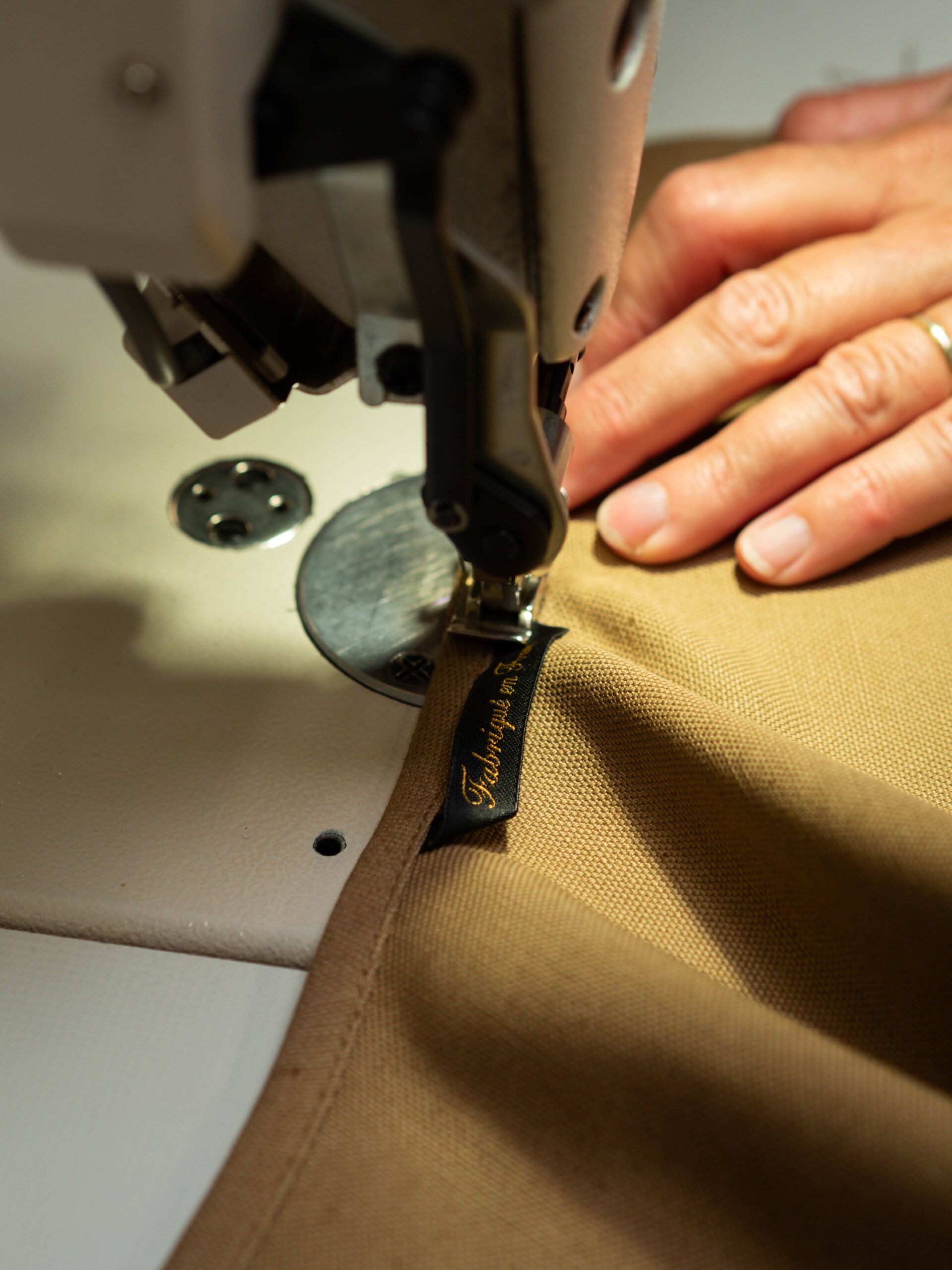 Pose à la machine de l’étiquette « Fabriqué en France » sur la toile brune du tablier dans l’atelier Le Laboureur.