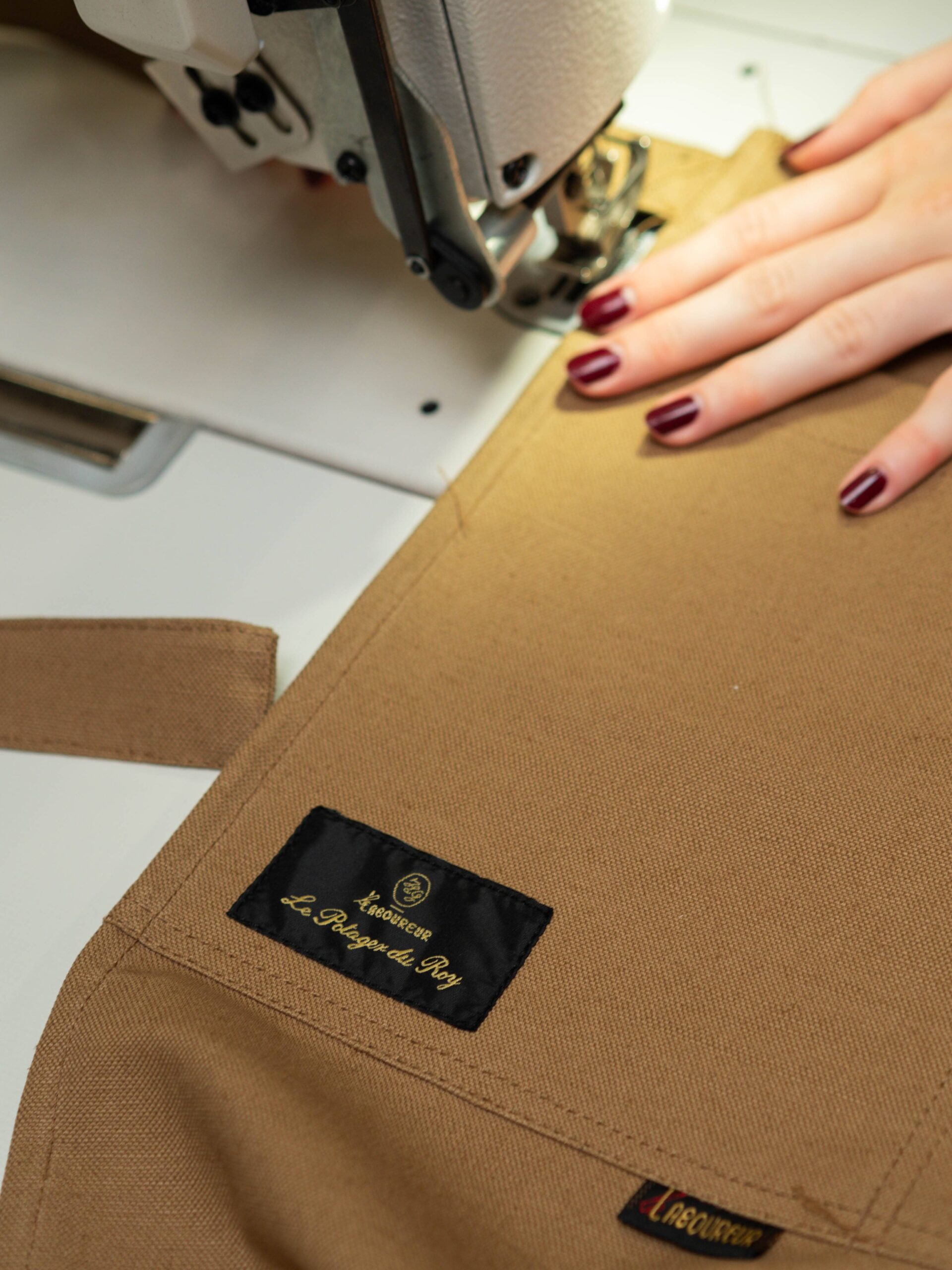 Couture du tablier en toile brune à la machine dans l’atelier Le Laboureur, près de l’étiquette Le Potager du Roy.