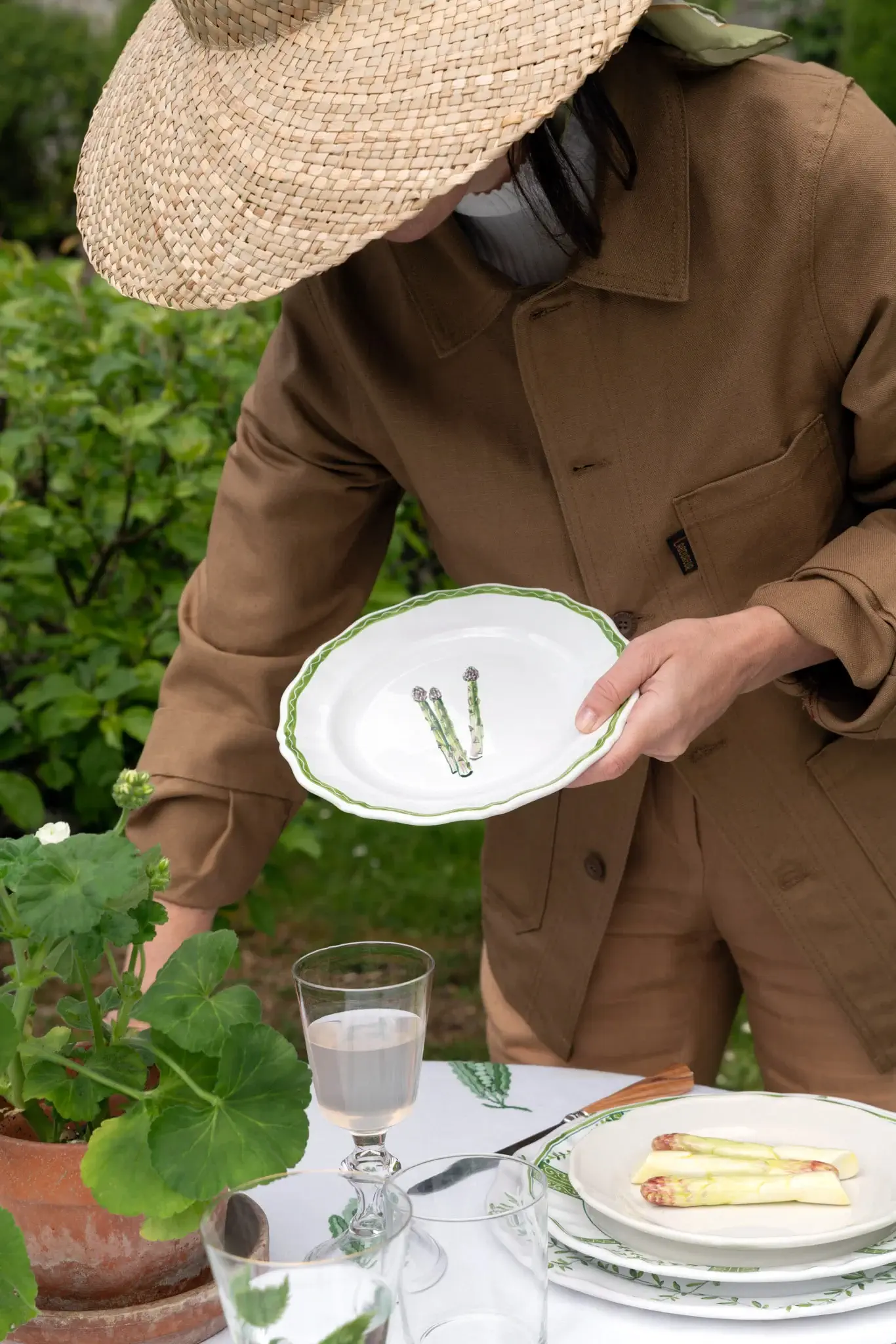 Veston brun Le Potager du Roy x Le Laboureur porté dans un jardin par une personne qui dresse une table.